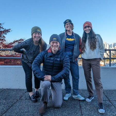 four people standing and smiling for a photo each wearing PSF branded touques